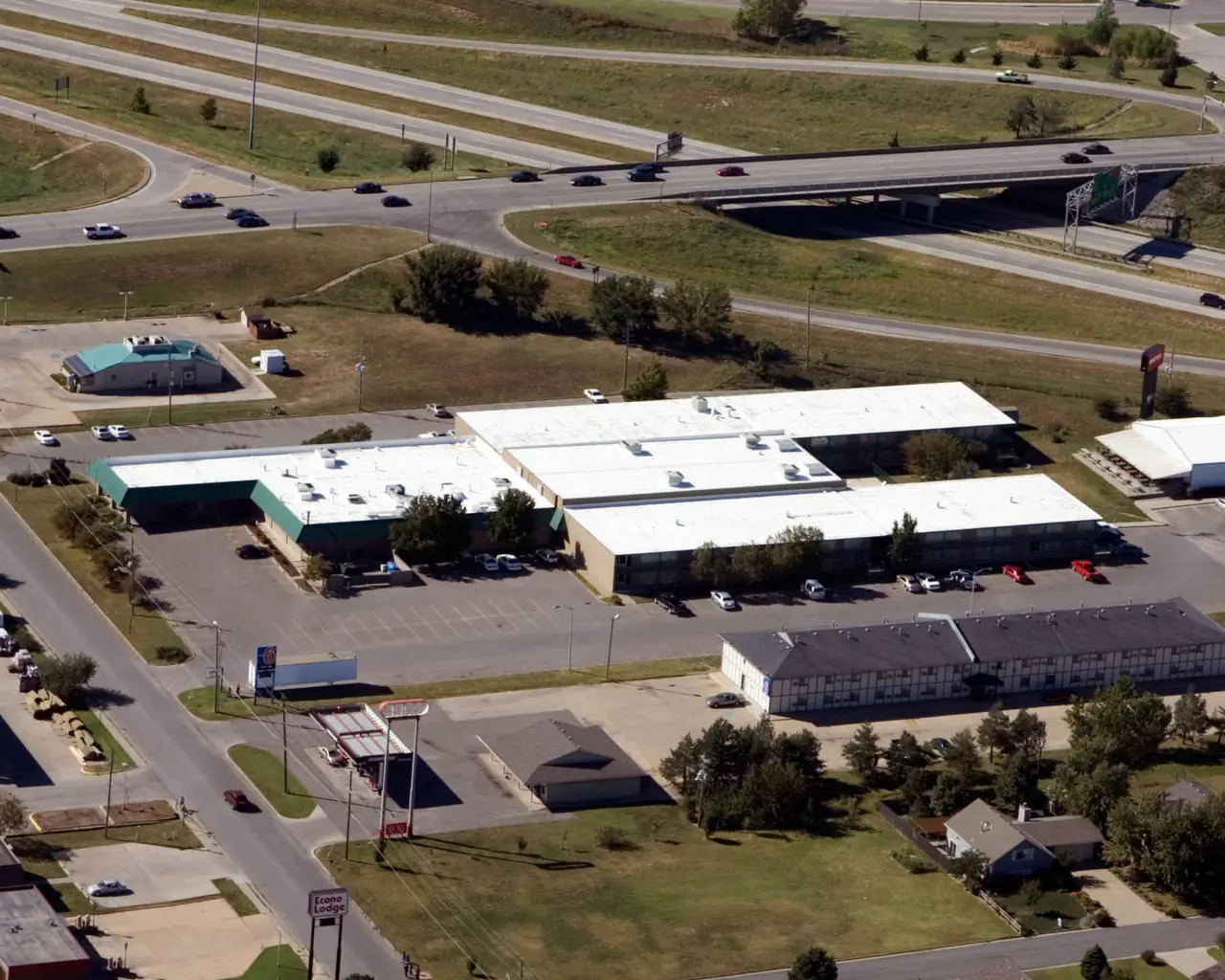 Aerial view of low commercial buildings with white roofs beside a highway interchange