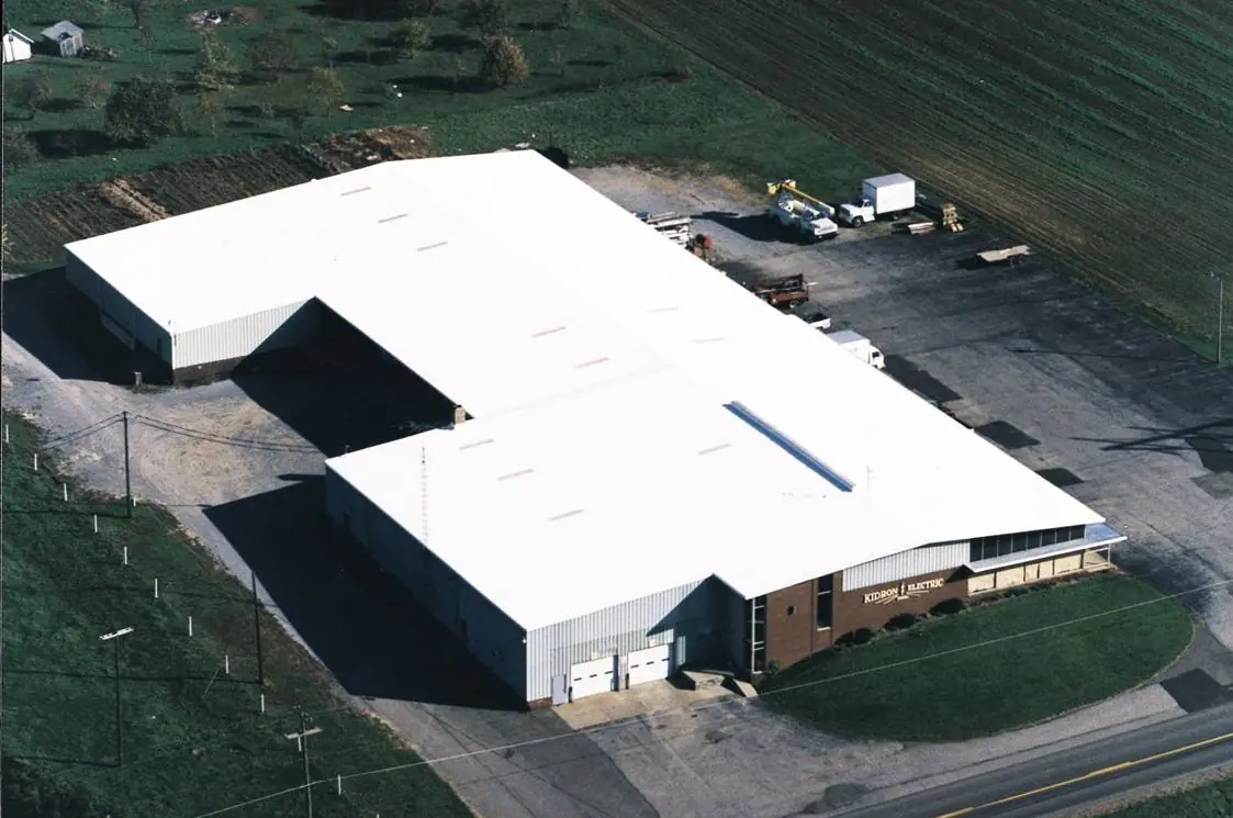 Aerial view of a manufacturing building with a seamless white roof in a rural setting