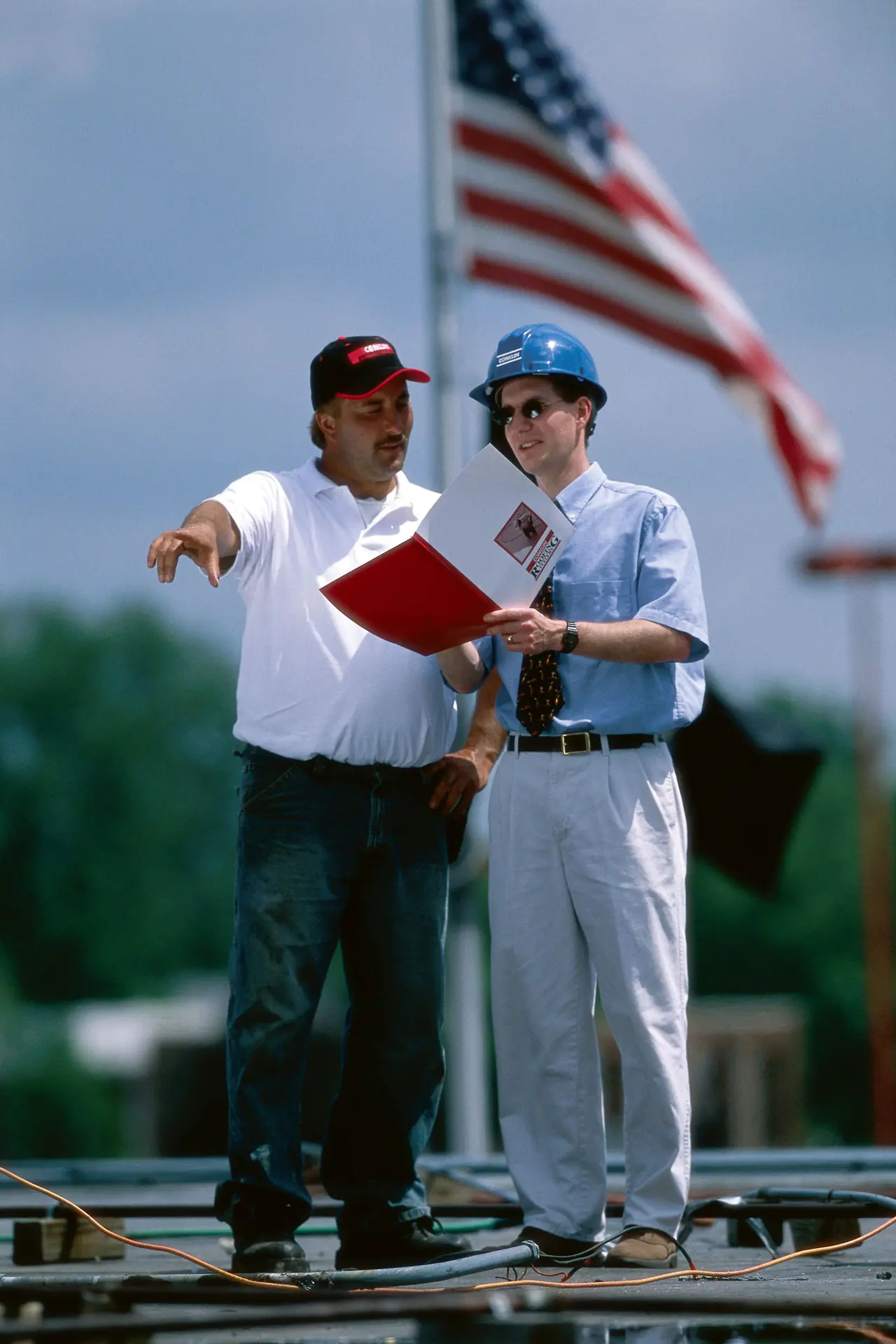A roofing contractor pointing out roof conditions to a building representative holding a report