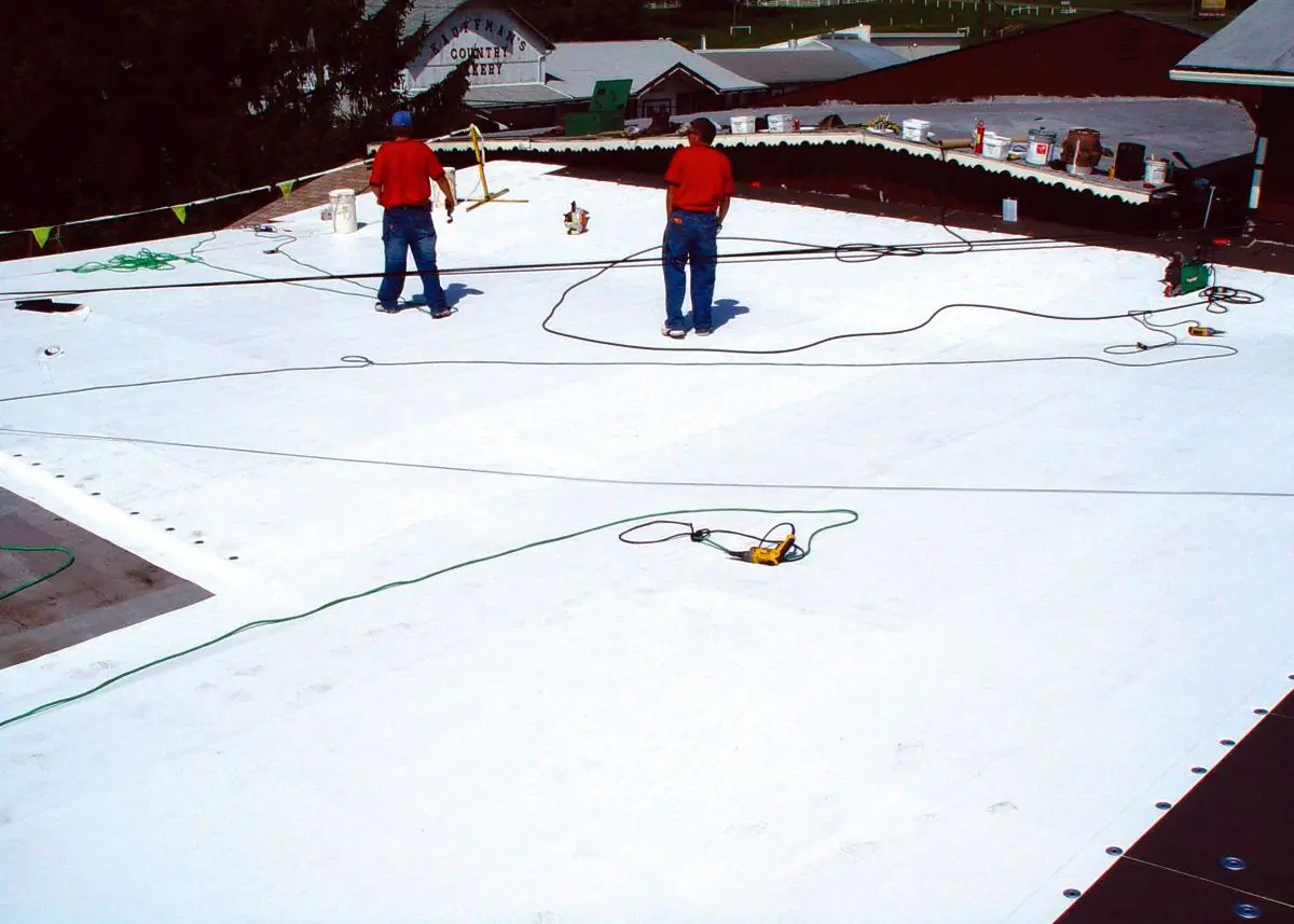 Two roofers applying a white coating across a large flat commercial roof