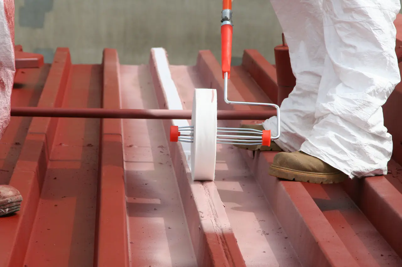 Close view of a roller applying coating along the ribs of a red metal roof