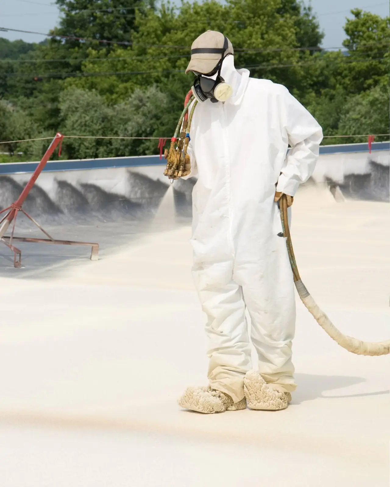 A worker in a protective suit and respirator spraying polyurethane foam on a flat roof