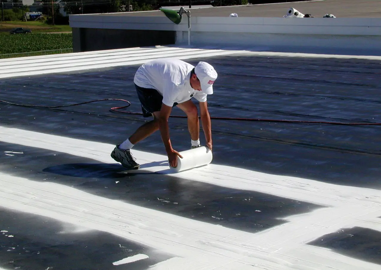 A roofer unrolling reinforcing fabric over the seams of a dark flat roof